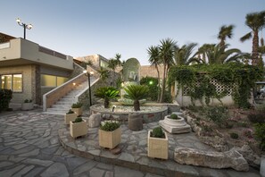 A courtyard with a stone floor, a central planter with plants, a staircase, and a building with a modern design.