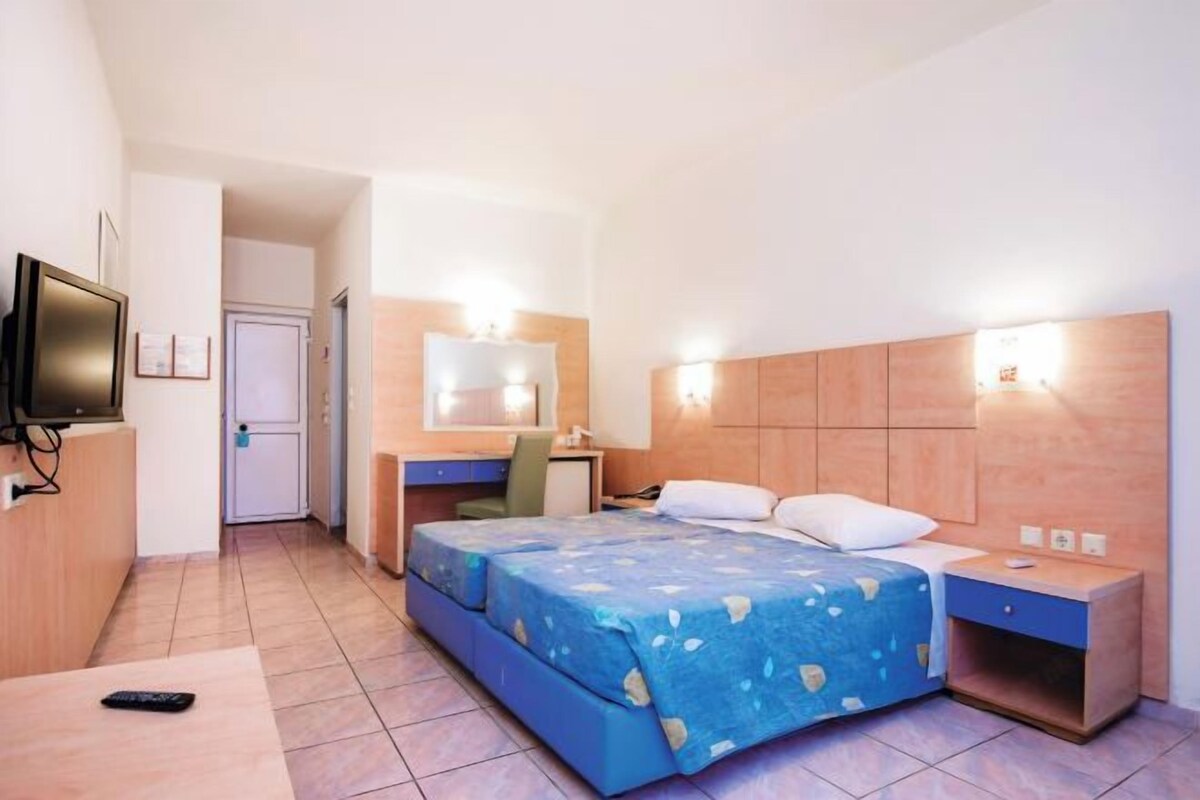 A hotel room with a bed, bedside table, desk, chair, and a television.