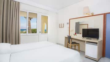 Habitación de hotel con cama, escritorio con televisor, refrigerador pequeño y ventana con vista al mar.