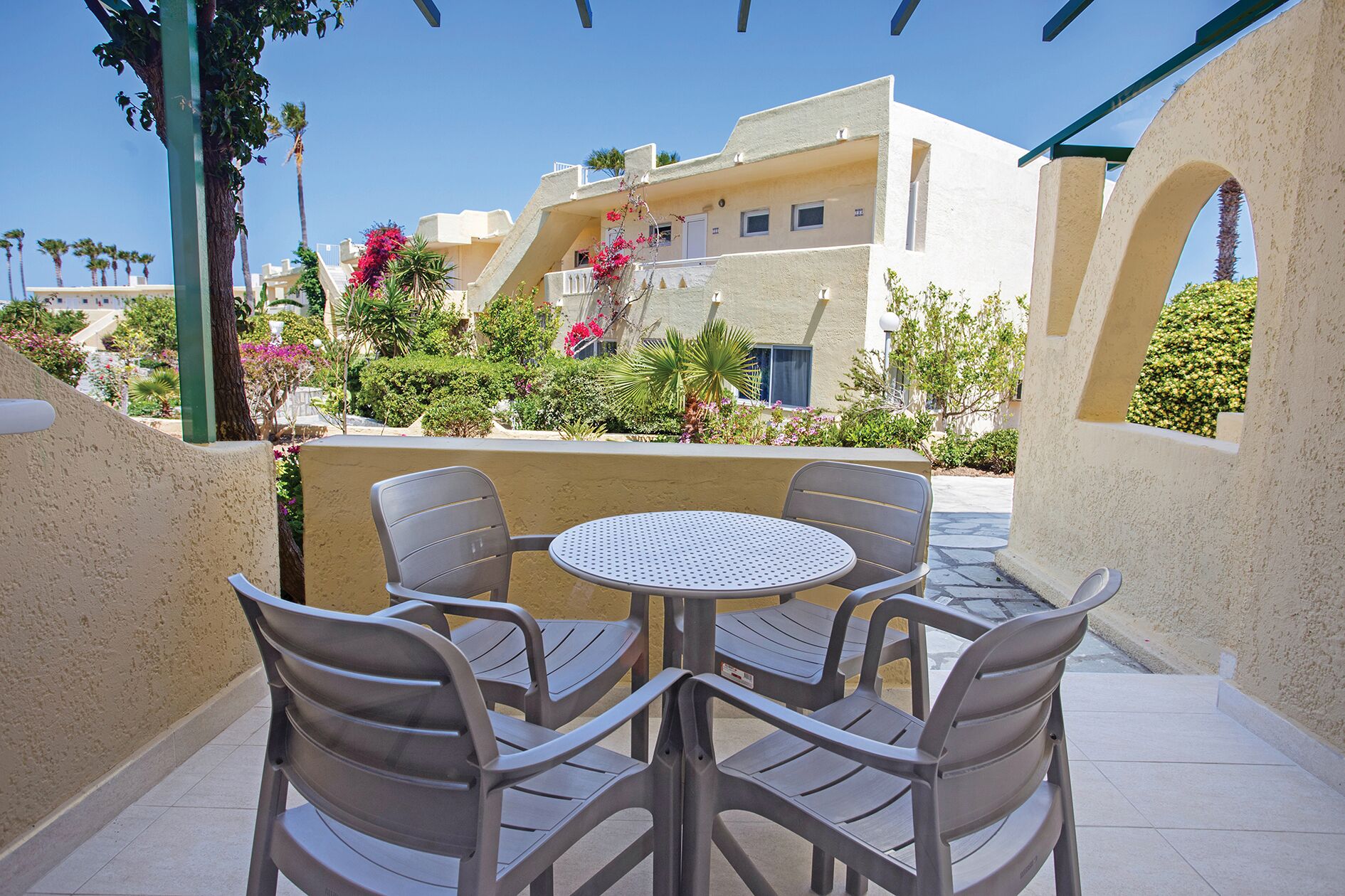 Eine Terrasse mit rundem Tisch und vier St ühlen, umgeben von beigen Wänden und üppiger Bepflanzung.