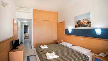 Quarto de hotel com cama, televisão, escrivaninha e guarda-roupa.