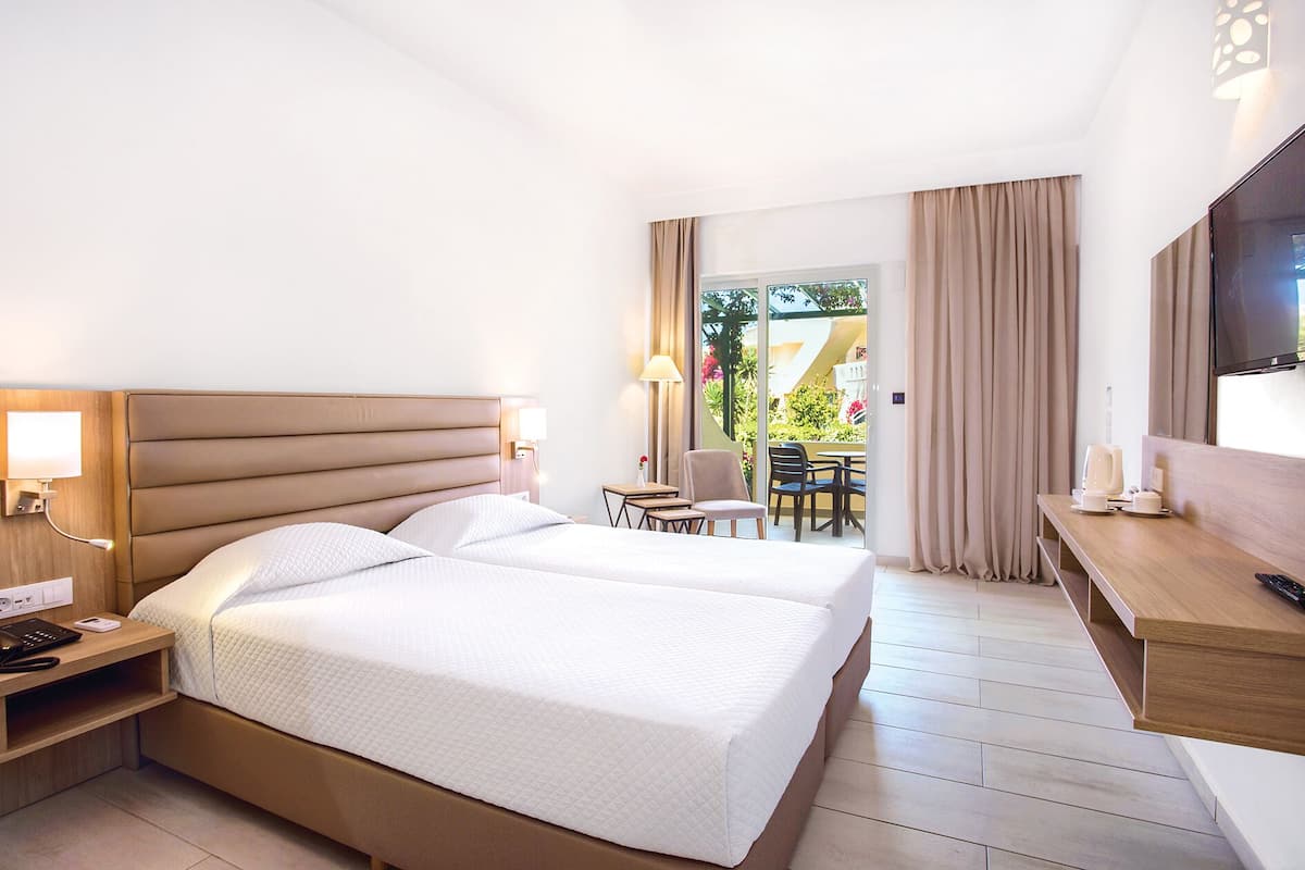 Une chambre d’hôtel avec un lit double, des tables de chevet, un bureau avec une chaise, une télévision et un balcon avec des rideaux.