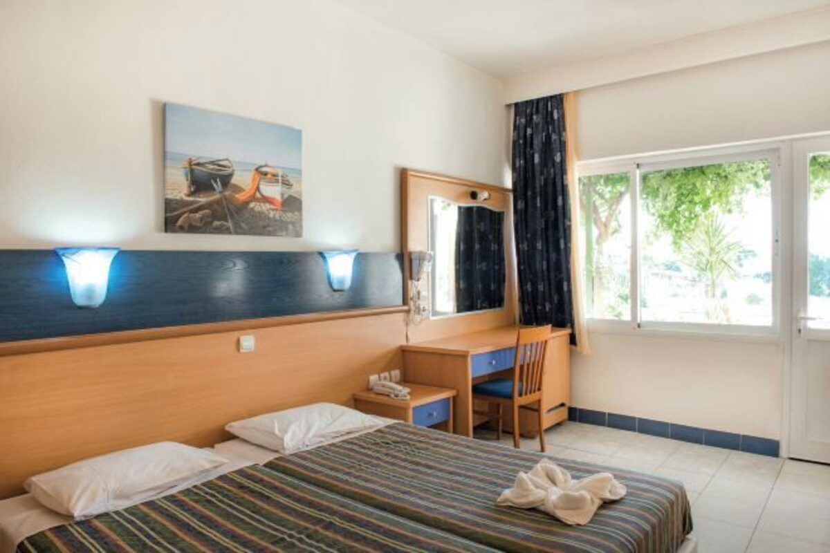 A hotel room with a bed, desk, chair, and a window with curtains.