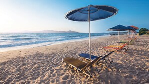 Une plage bordée de rangées de chaises longues et de parasols, une étendue de sable et l’océan en toile de fond.