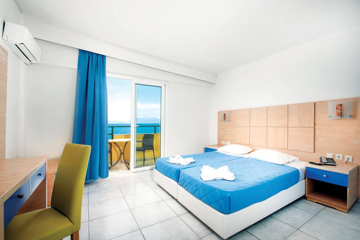 Une chambre d’hôtel avec un lit, un bureau, une chaise, une table de chevet et une vue sur la mer.