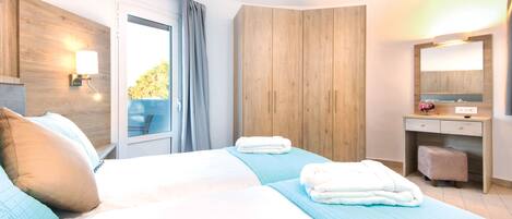 Habitación de hotel con dos camas, un armario de madera, un baño con espejo y lavabo, y una ventana con cortinas.