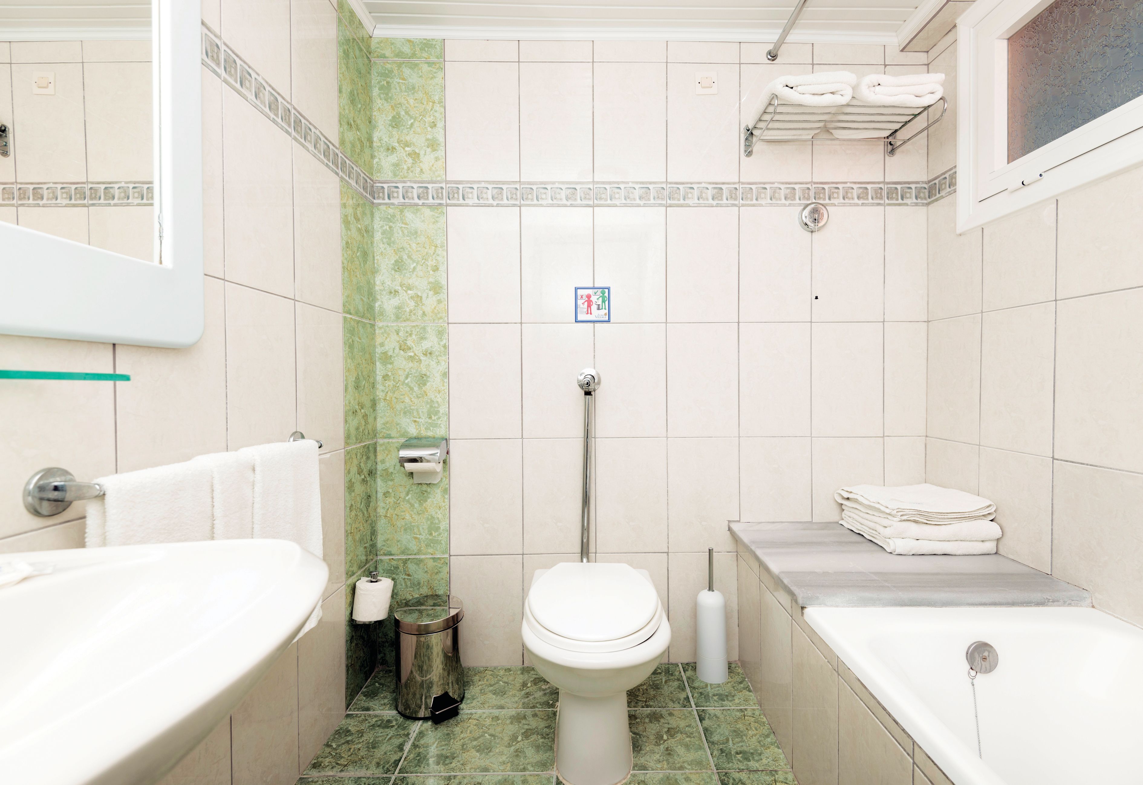 Un baño con inodoro, lavabo y bañera. Hay toallas apiladas en la pared y un cubo de basura.