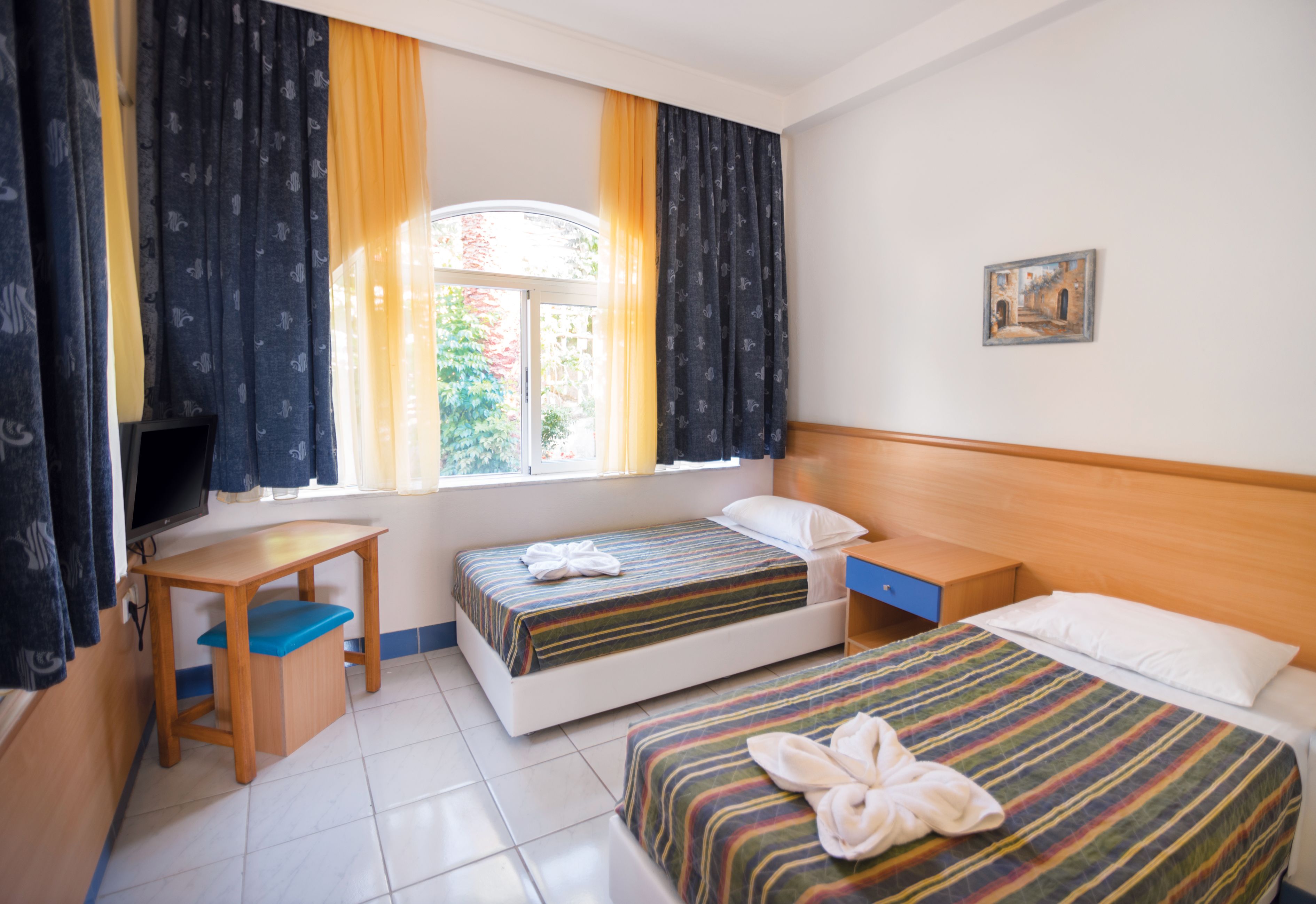 A hotel room with two beds, a desk, and a window with curtains.
