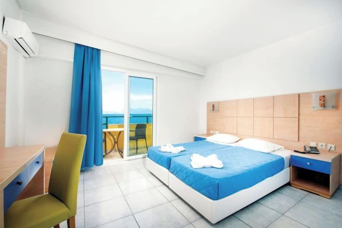 A hotel room with a bed, a desk, a chair, a small table, and a view of the outdoors.