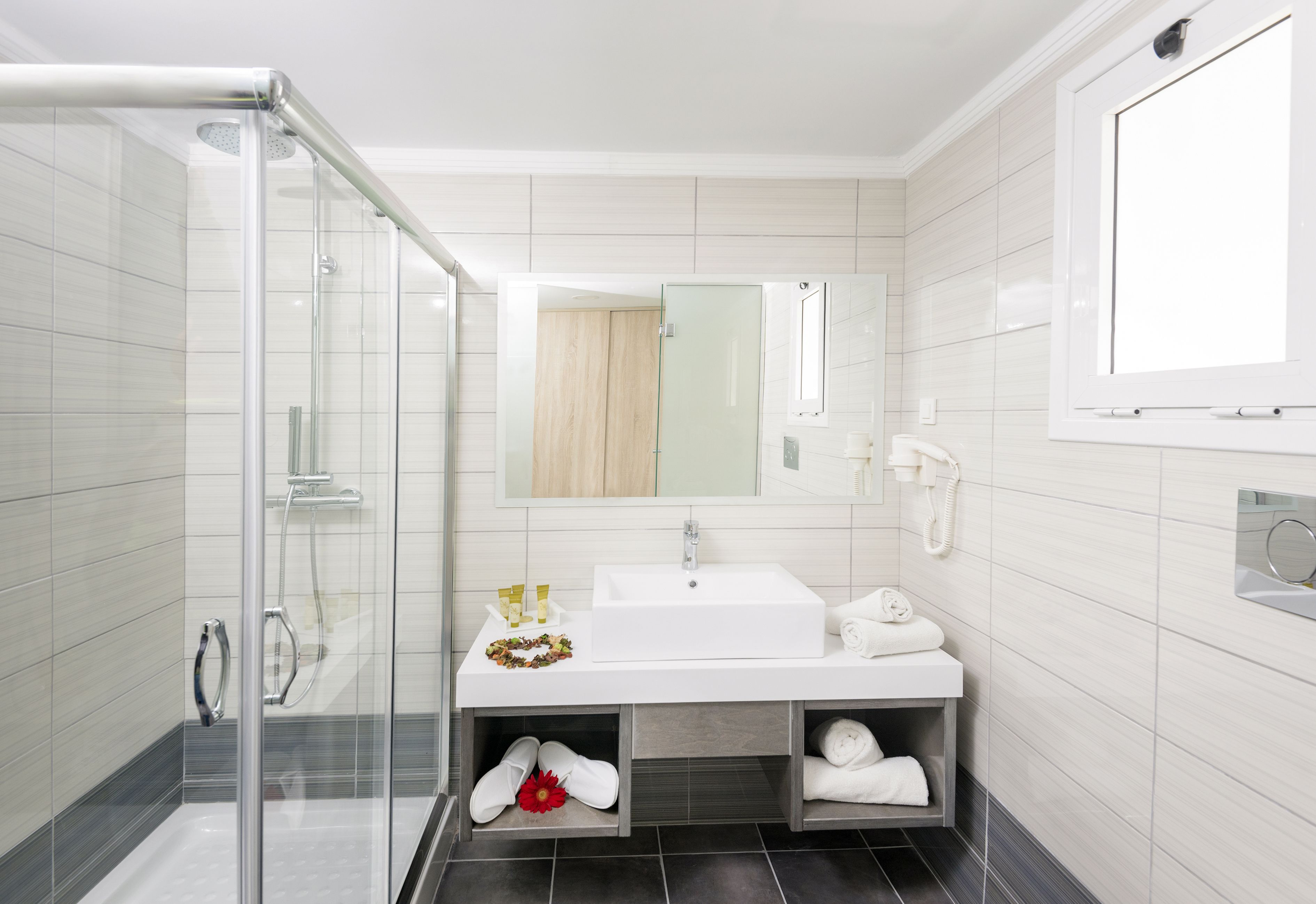 A modern bathroom with a glass shower enclosure, a white sink, and a mirror above it.