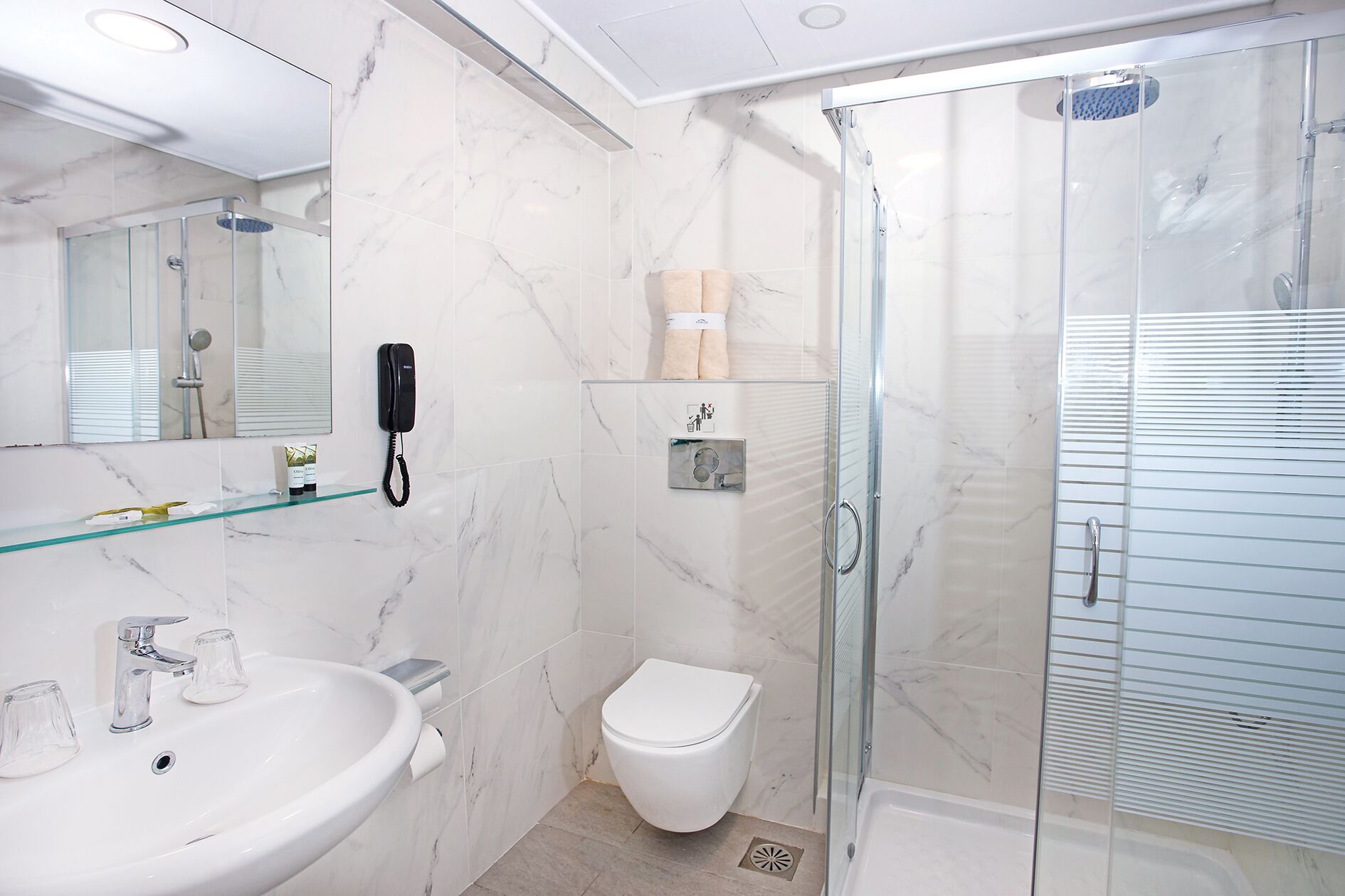 Ein modernes Badezimmer mit Duschkabine aus Glas, einer weißen Toilette und einem Waschbecken aus Glas mit Marmorablage.
