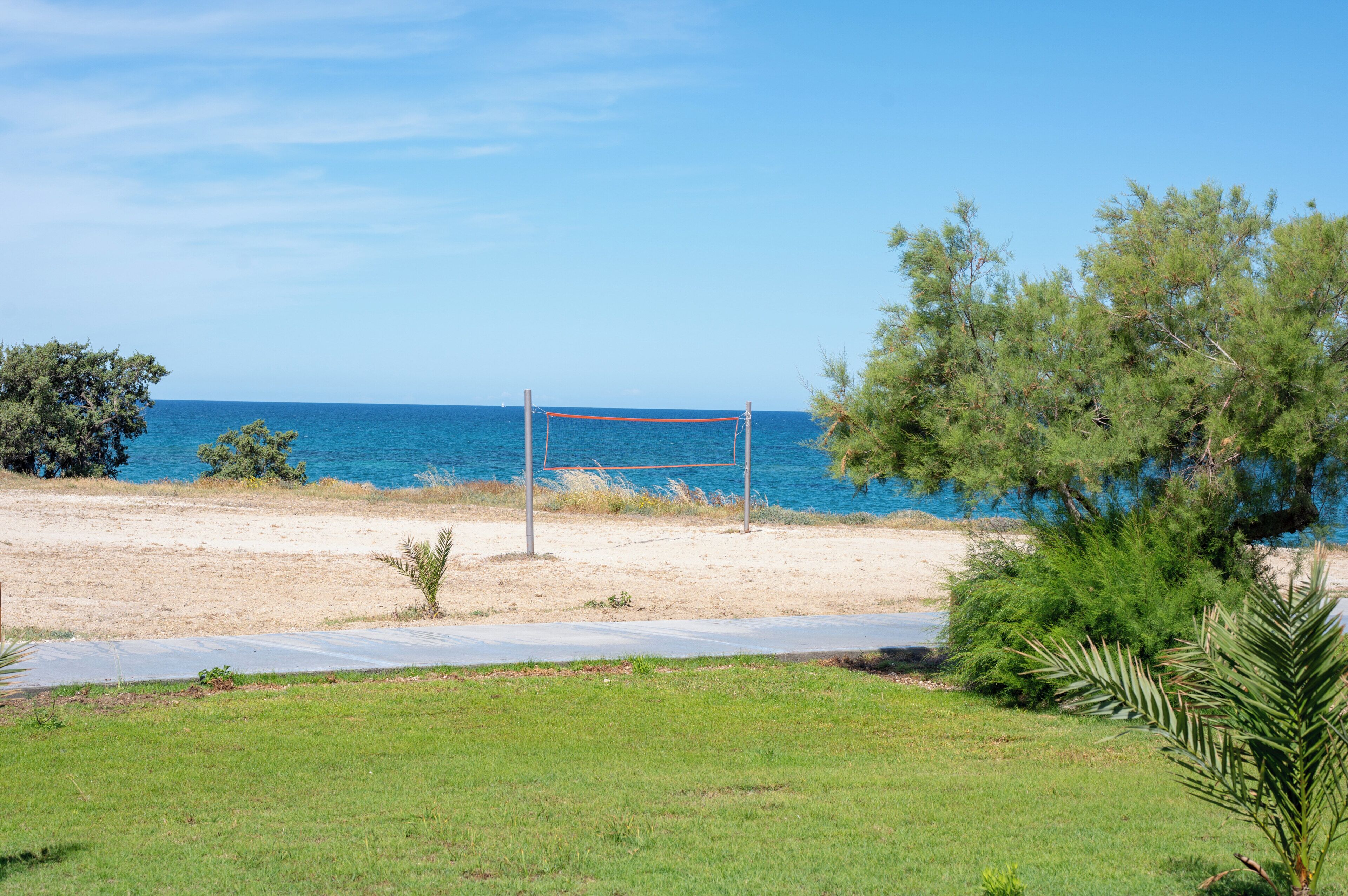 A beach volleyball net, a sandy beach, and a clear blue sky.