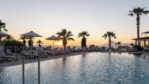 A pool area with lounge chairs and umbrellas, palm trees, and a sunset in the background. - Kouros Palace Active Lifestyle Hotel (Kos)