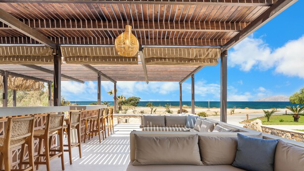 A covered outdoor seating area with a view of the ocean, a bar, and a sofa. - Kouros Palace Active Lifestyle Hotel (Kos)