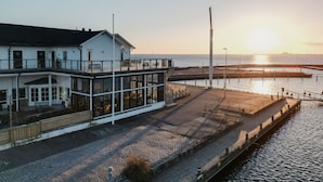 En bygning ved vandet med en glasfacade, en overdækket terrasse og udsigt til solnedgangen over vandet.