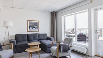 Una sala de estar moderna con un sofá gris, una mesa de centro de madera y un sillón gris. Hay un ventanal con vistas al exterior.