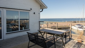En træterrasse med bord og stole, med udsigt over en lysthavn med både og en strand.