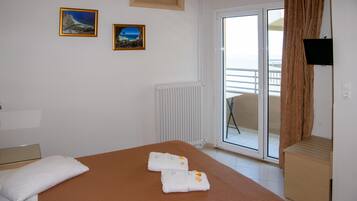 Una camera d'albergo con un letto, due quadri appesi al muro, un termosifone e una porta scorrevole in vetro che dà su un balcone.