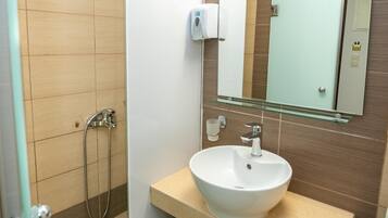 A bathroom with a white sink, a glass shelf, a handheld soap dispenser, and a shower with a handheld showerhead.