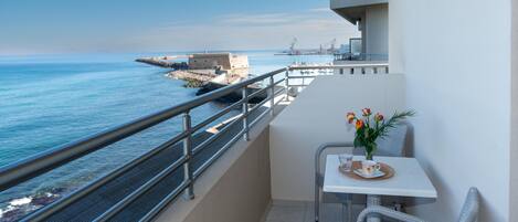 A balcony with a view of the sea, a table with a vase of flowers, and a chair.