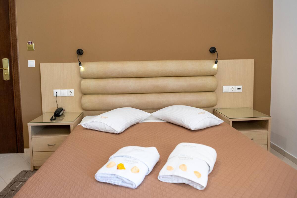 Une chambre d’hôtel comprenant un lit, deux tables de chevet, une petite table, une lampe fixée au mur et un téléphone.