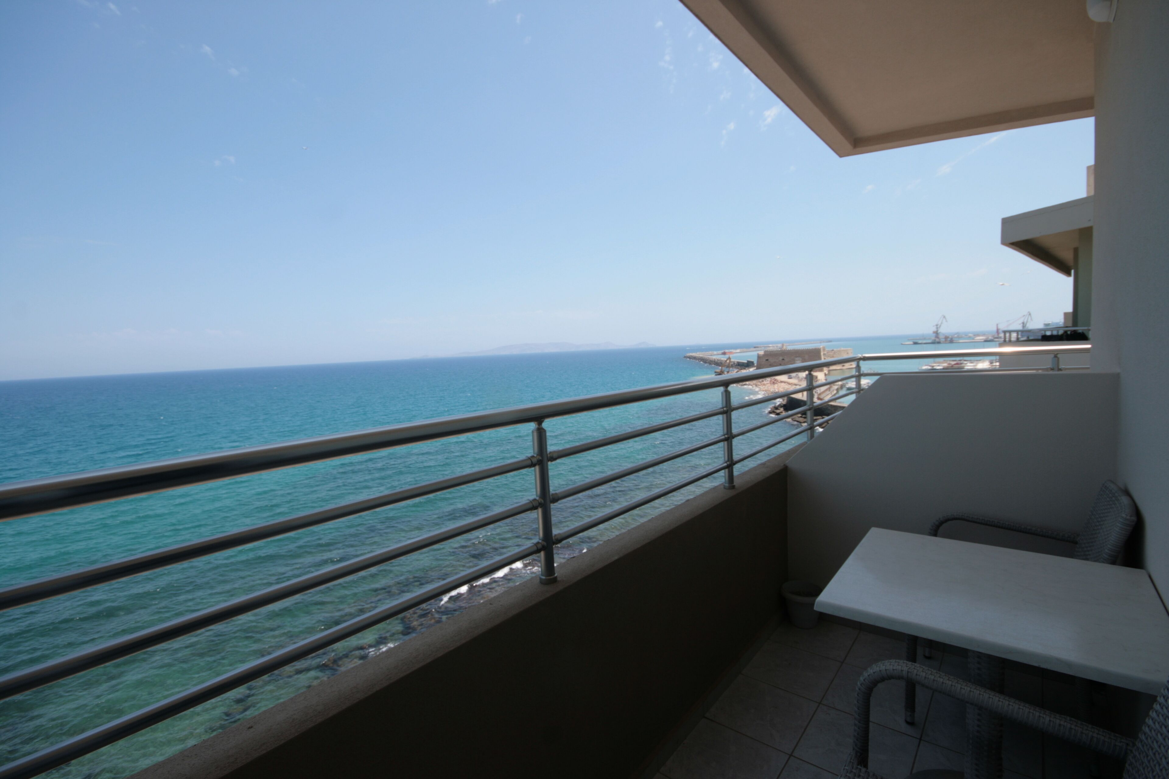 A balcony with a view of the sea, a white table, and a wicker chair.