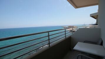 A balcony with a view of the sea, a white table, and a wicker chair.