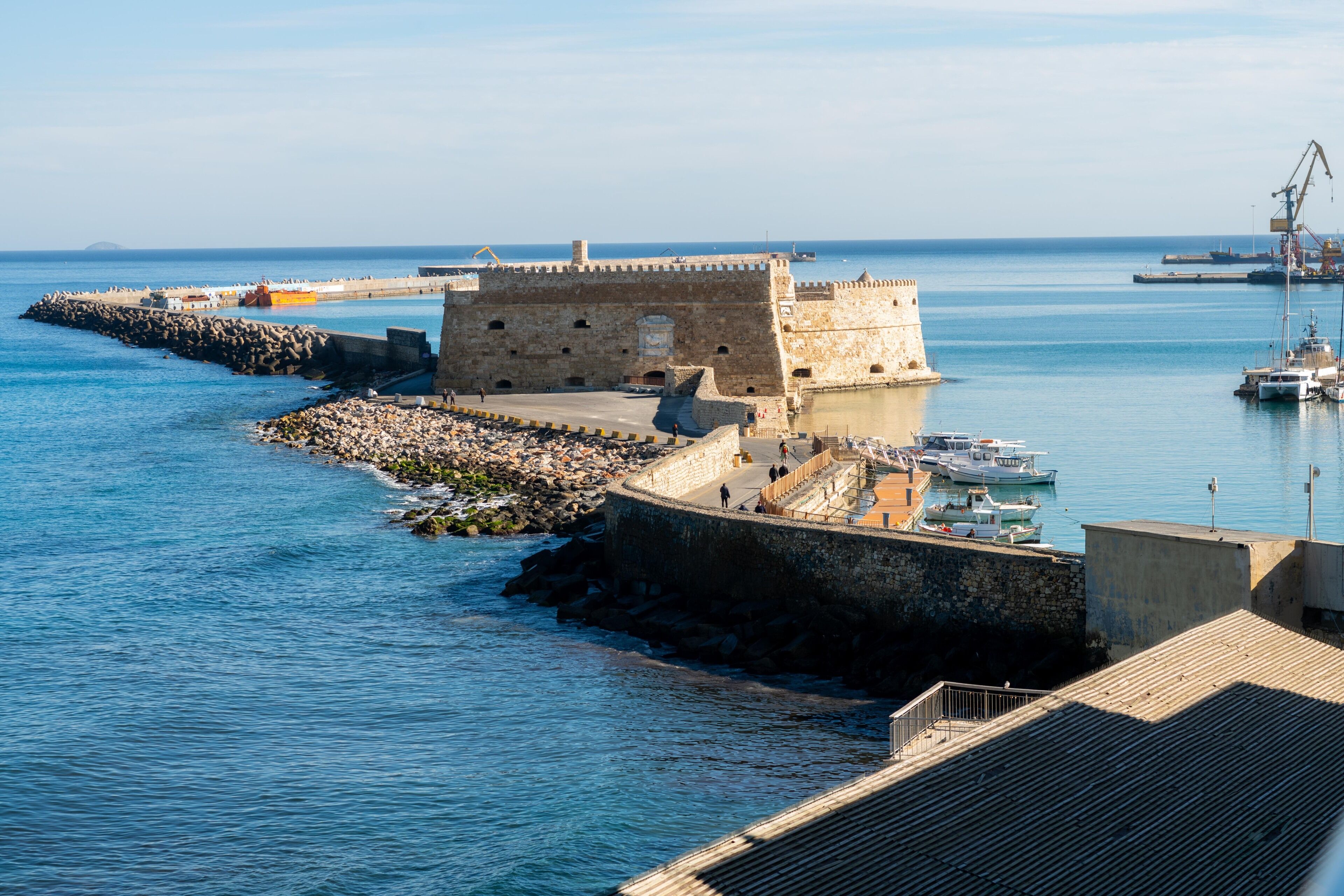 Una fortificazione costiera con un muro di pietra, un molo di legno e barche nell'acqua.
