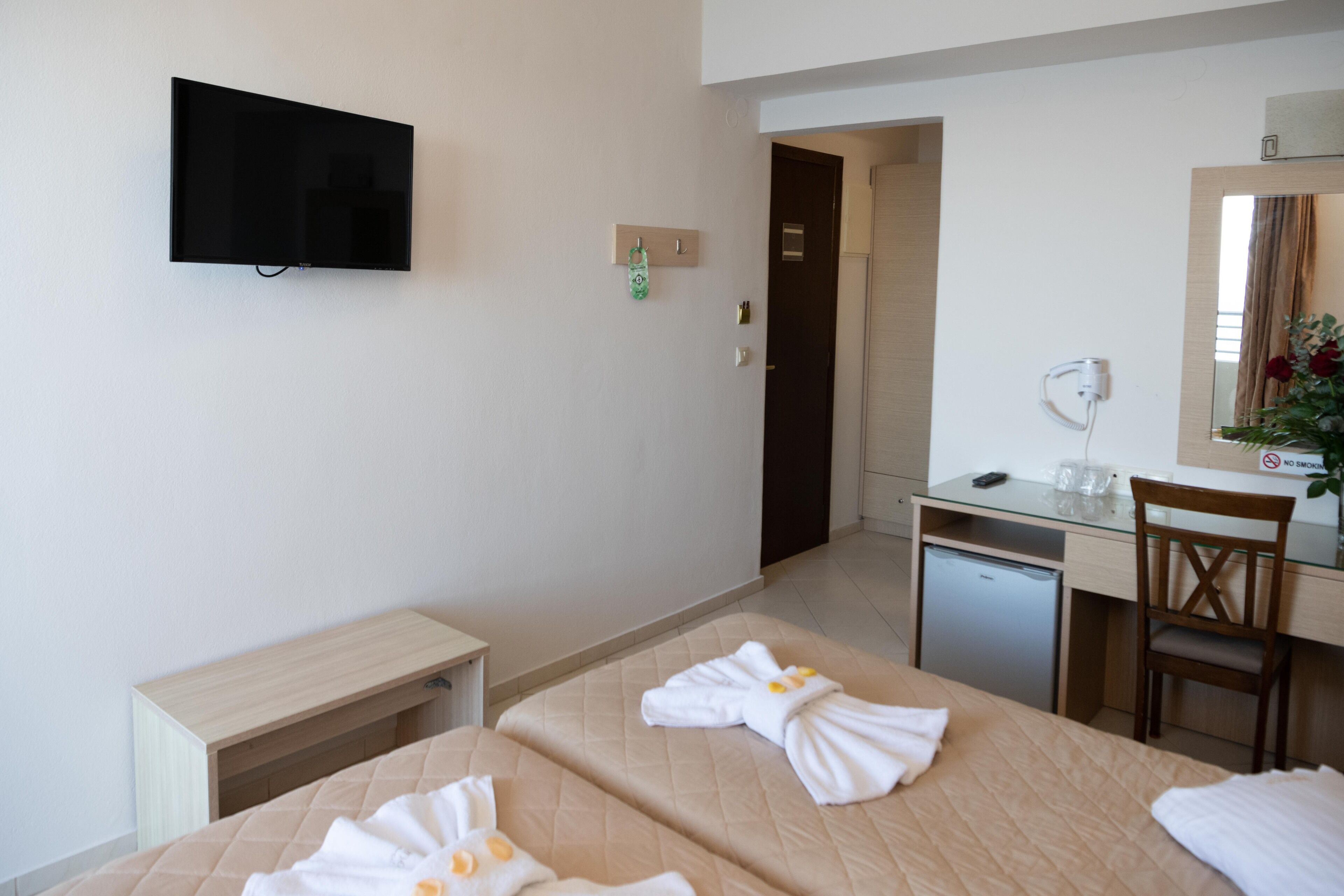 Habitació d'hotel amb dos llits, una escriptori, una cadira, un televisor i un frigorífic petit.
