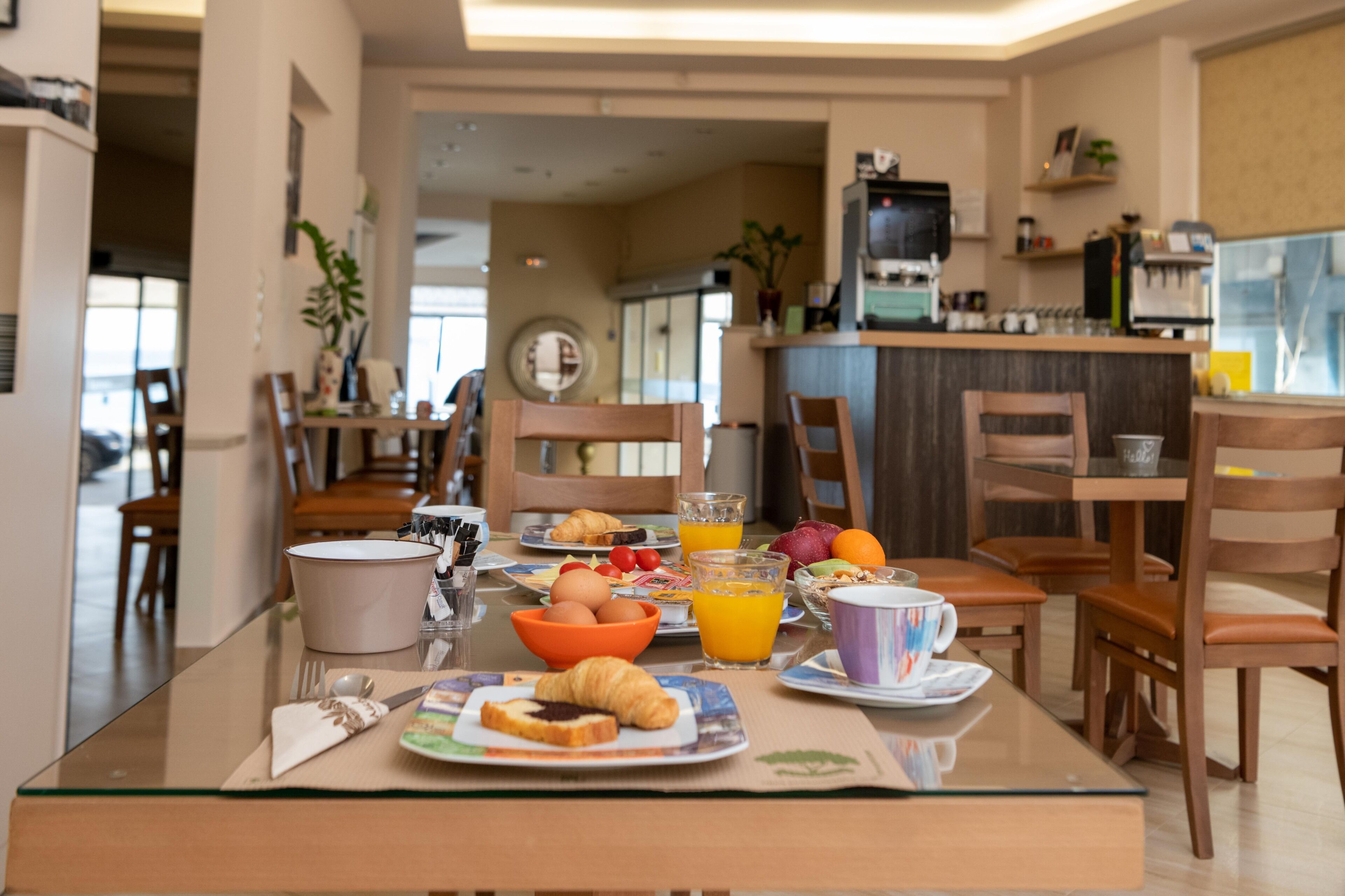 Un desayuno con una mesa preparada para dos personas, que incluye croissants, fruta y zumo de naranja.