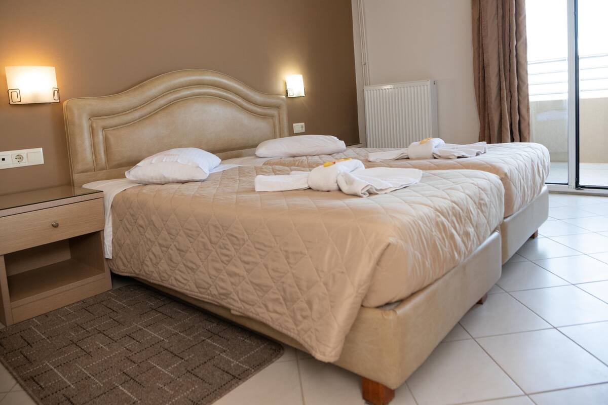 Une chambre d’hôtel avec deux lits, une table de chevet, une lampe et une vue sur l’extérieur.