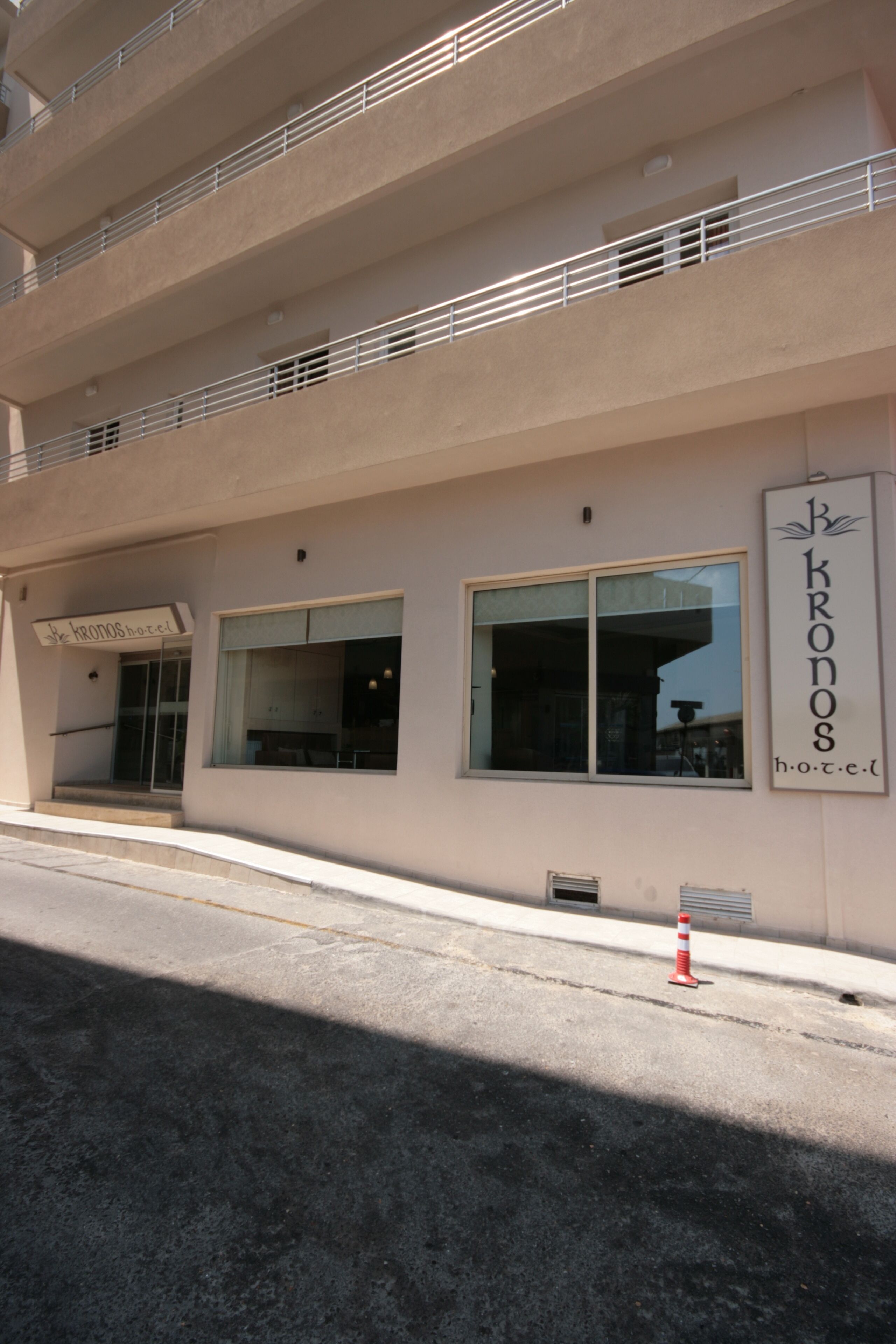 A hotel named "Kronos Hotel" with a modern facade, large windows, and a visible entrance.