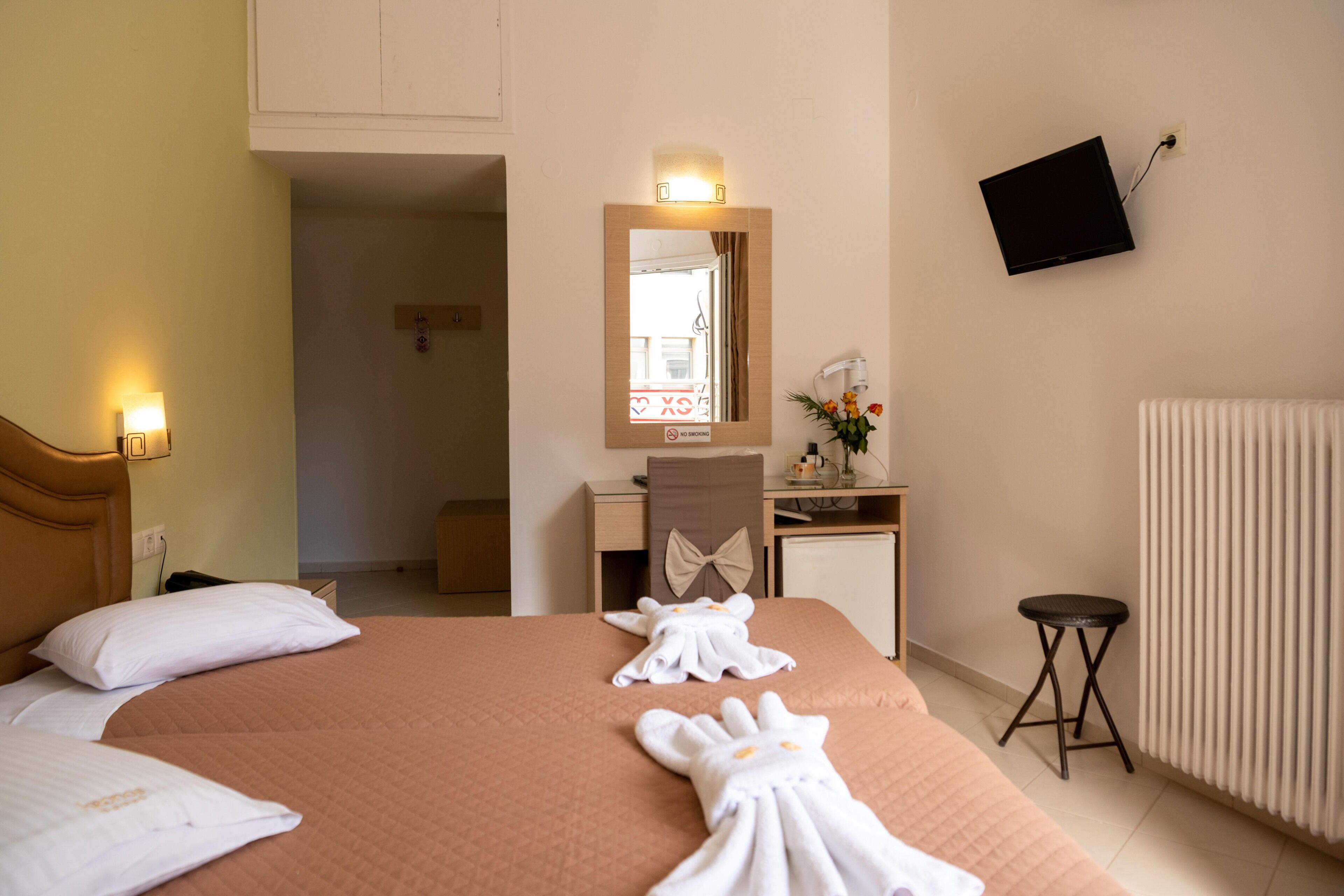 Habitación de hotel con cama, escritorio, silla, televisor montado en la pared y radiador.