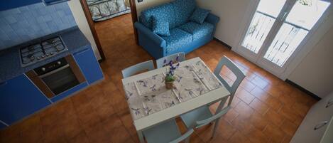 Una cocina compacta con armarios azules y una estufa a gas, un comedor con mesa y sillas, y un sofá azul con estampado.