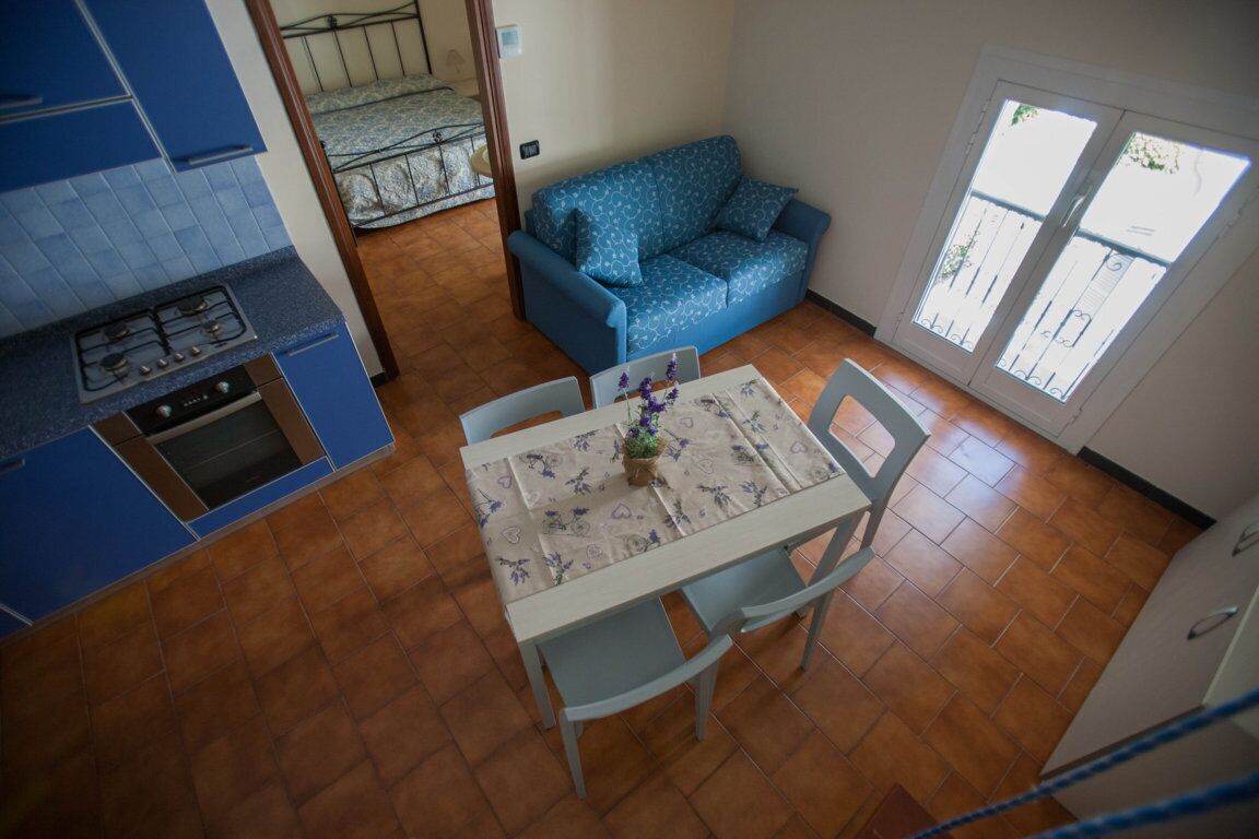 Eine kleine Küche mit blauen Schränken, einem Esstisch mit Stühlen, einem blau gemusterten Sofa und einem Fenster mit Blick.