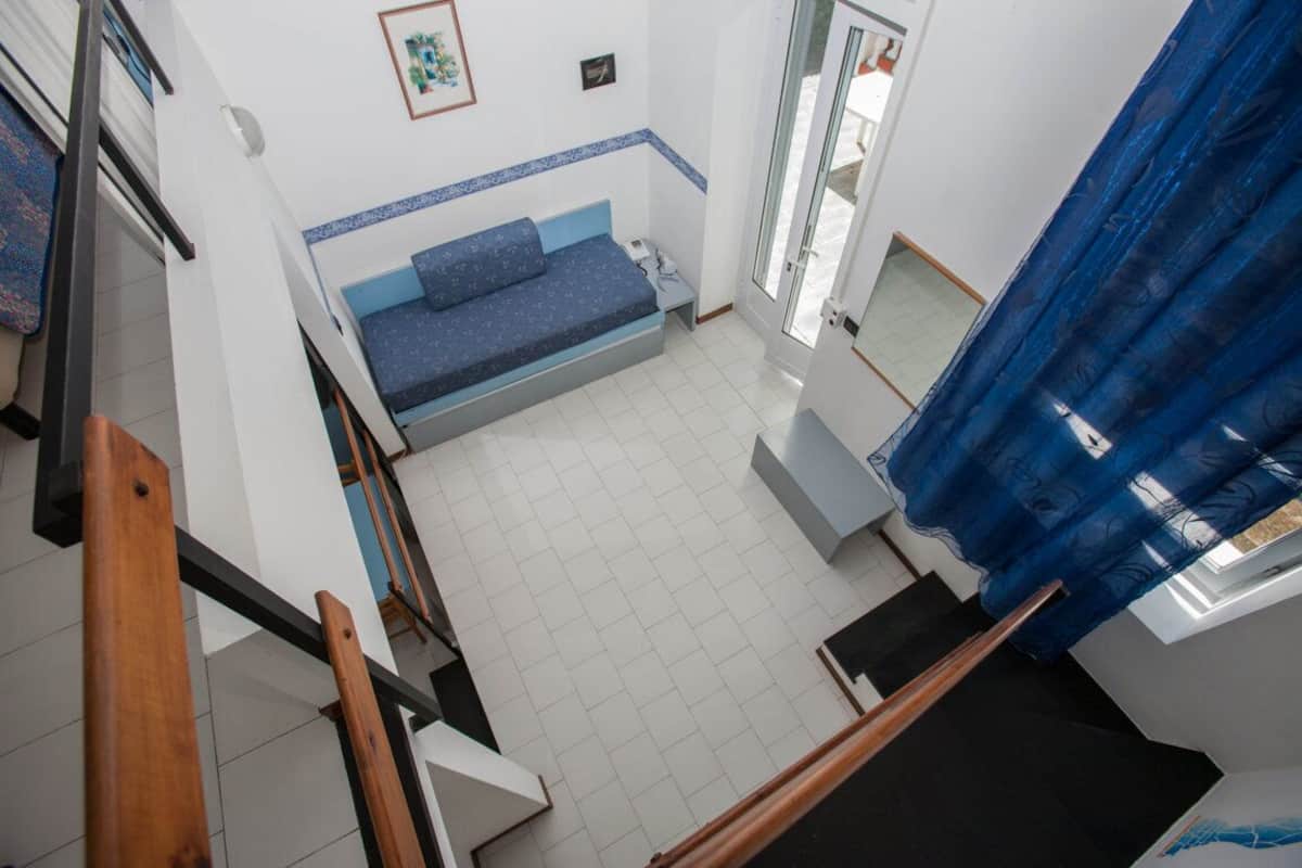 Una habitación con una cama, una mesita, una ventana con cortina y una escalera.