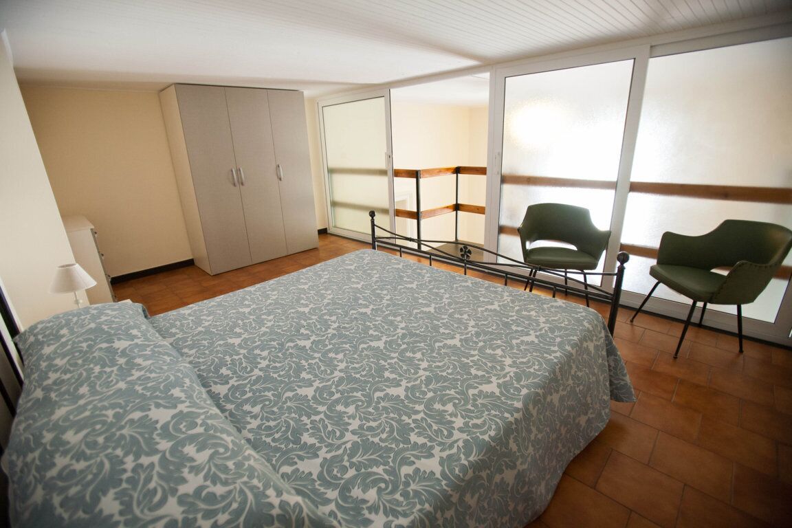 Ein Schlafzimmer mit Bett, Kleiderschrank, Stuhl und einem Balkon mit Blick.