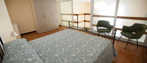 Ein Schlafzimmer mit Bett, Kleiderschrank, Stuhl und einem Balkon mit Blick.