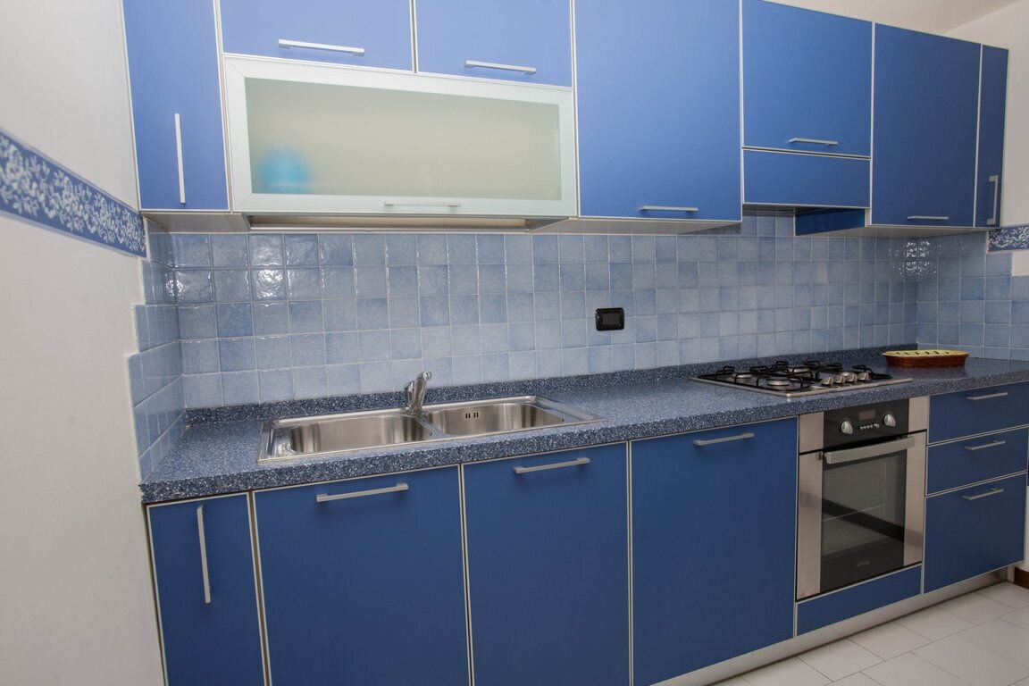 Une cuisine avec des meubles de couleur bleue, un évier en acier inoxydable, un four à micro-ondes, une cuisinière à gaz et un four traditionnel.