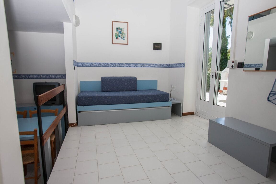 A compact room with a bed, a small table, a chair, and a television.
