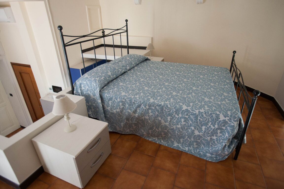 A bedroom with a bed, a bedside table with a lamp, a dresser, and a door.