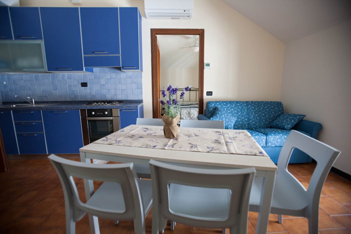 A compact kitchen with blue cabinets, a dining table with chairs, and a blue sofa in the living area.