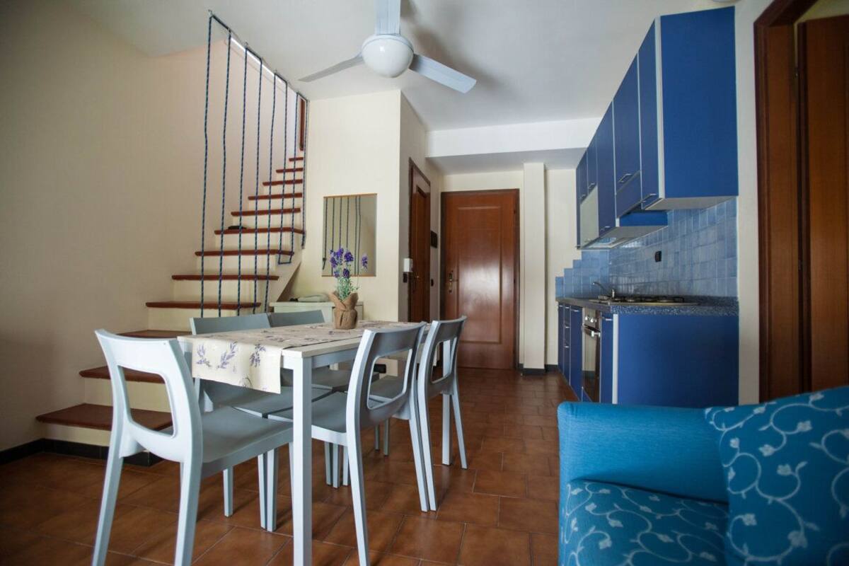 Un comedor con mesa y sillas, una cocina con armarios azules y una escalera.