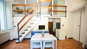 A kitchen with a wooden staircase, a dining table with chairs, and a small refrigerator. - Residence RTA Villa Marina (Imperia)