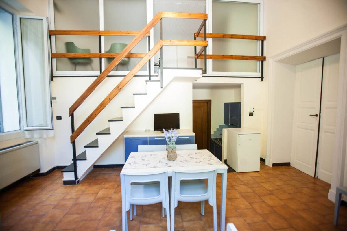 Una cocina con una escalera de madera, una mesa de comedor con sillas y un refrigerador pequeño.