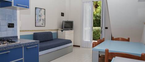 A compact room with a kitchenette, a bed, a TV, and a dining area.