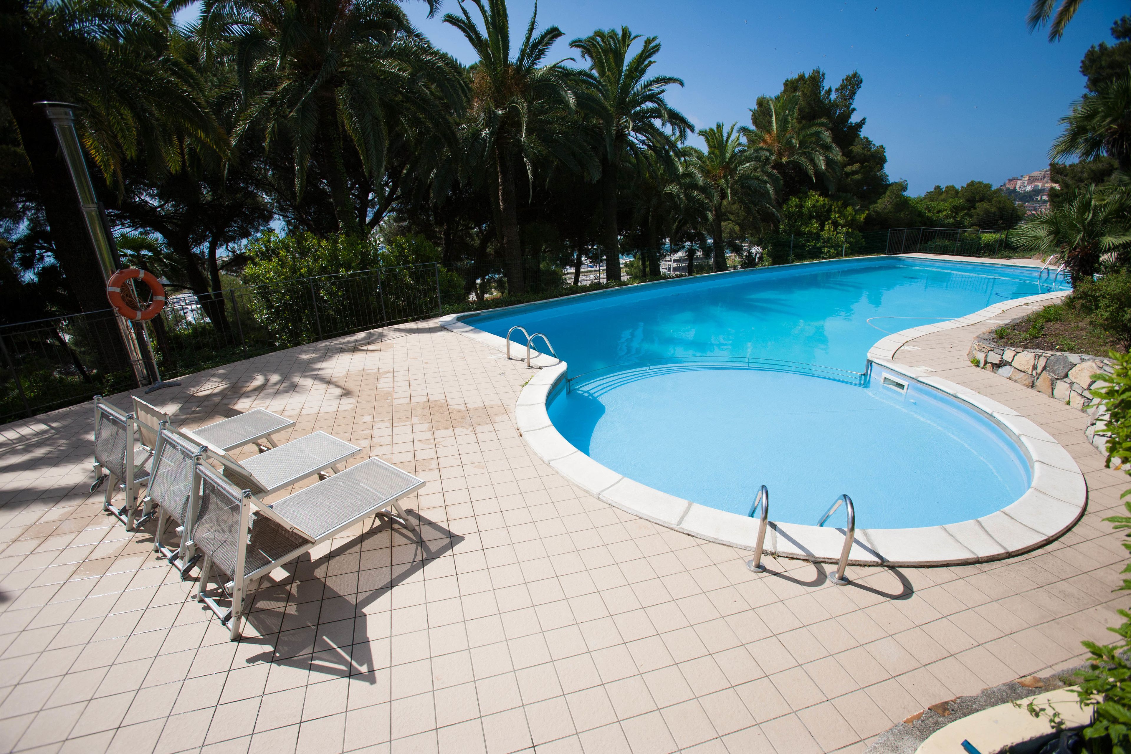 Une piscine avec une terrasse carrelée, des chaises longues et des palmiers en arrière-plan.