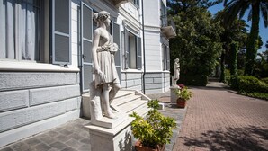A building with classical statues on the steps and a paved pathway. - Residence RTA Villa Marina (Imperia)