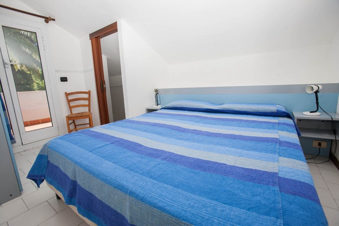A bedroom with a bed, a chair, a nightstand, and a door leading to a balcony.