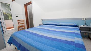 A bedroom with a bed, a chair, a nightstand, and a door leading to a balcony.